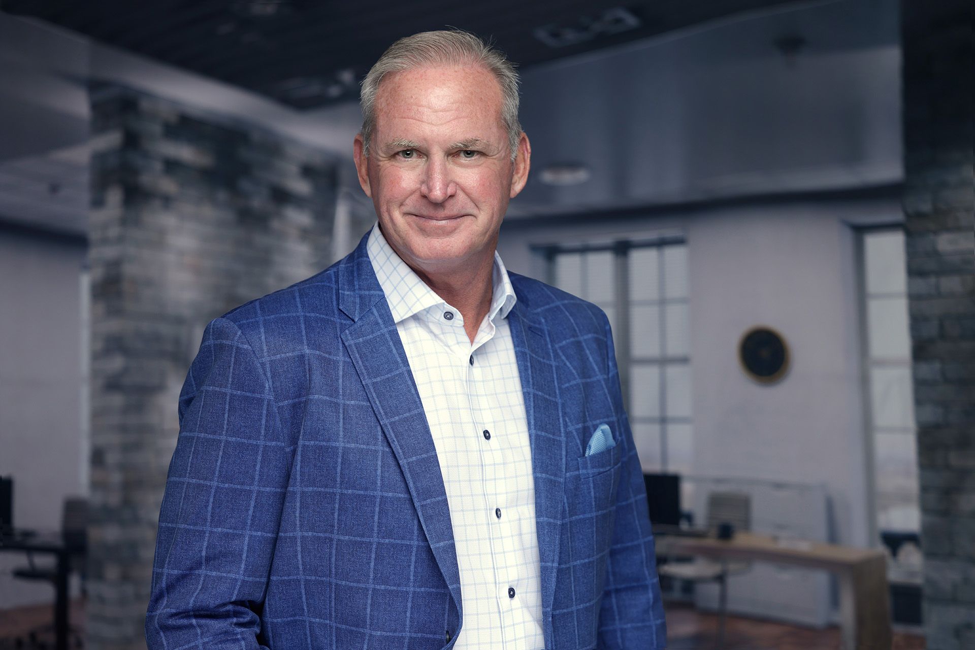 Professional branding headshot of a confident business executive in a blue checkered suit and white shirt, photographed in a modern office setting.